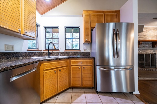 kitchen featuring light tile patterned floors, appliances with stainless steel finishes, vaulted ceiling, a sink, and dark stone countertops