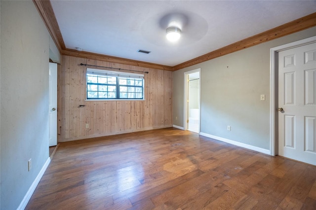 spare room featuring crown molding, wood finished floors, visible vents, and baseboards