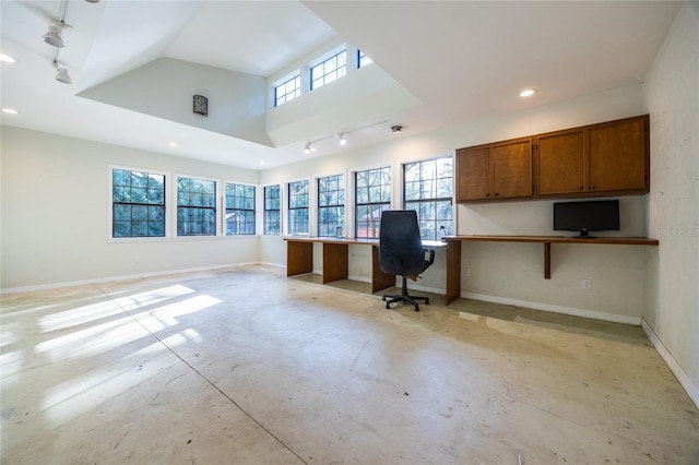 unfurnished office featuring rail lighting, built in study area, baseboards, and unfinished concrete floors