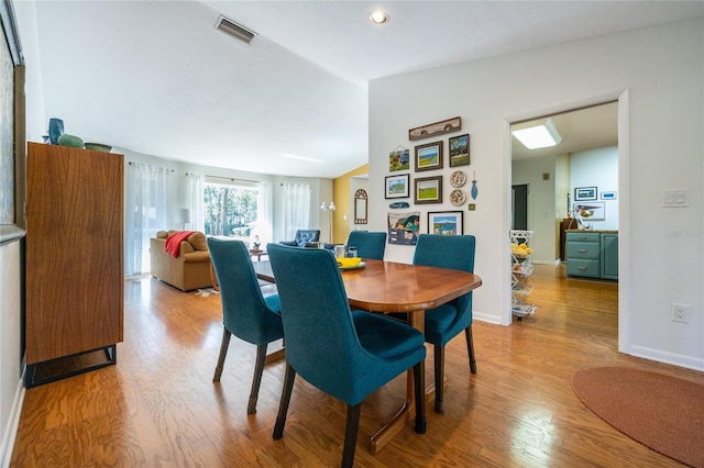 dining space with visible vents, lofted ceiling, baseboards, and wood finished floors