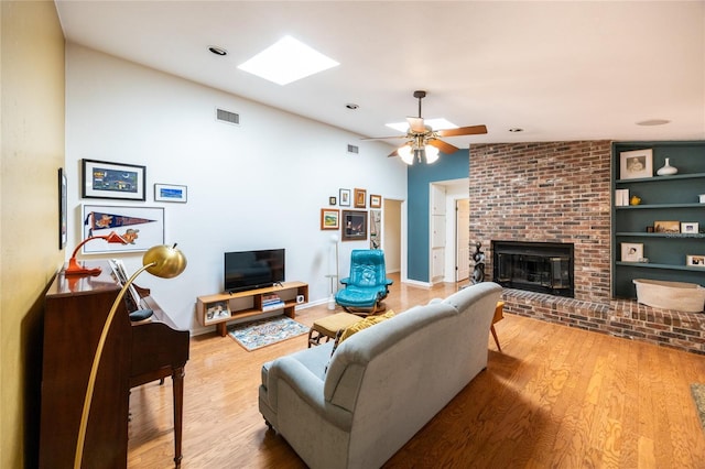 living area featuring vaulted ceiling with skylight, a brick fireplace, wood finished floors, and visible vents