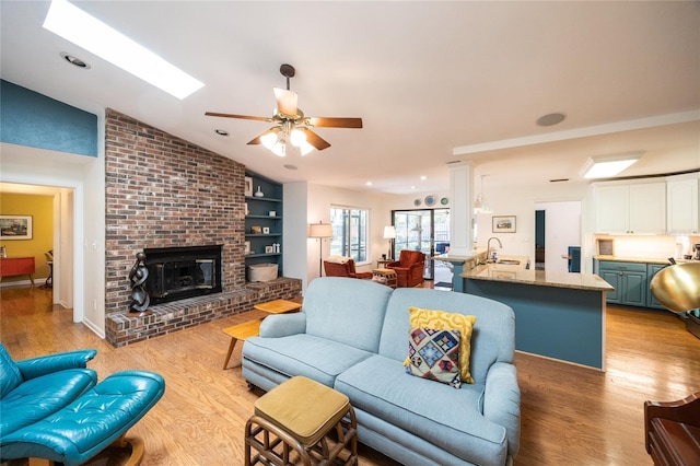 living room featuring light wood-style flooring, a ceiling fan, recessed lighting, vaulted ceiling with skylight, and a brick fireplace