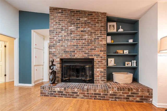 unfurnished living room with a fireplace, baseboards, built in shelves, and wood finished floors