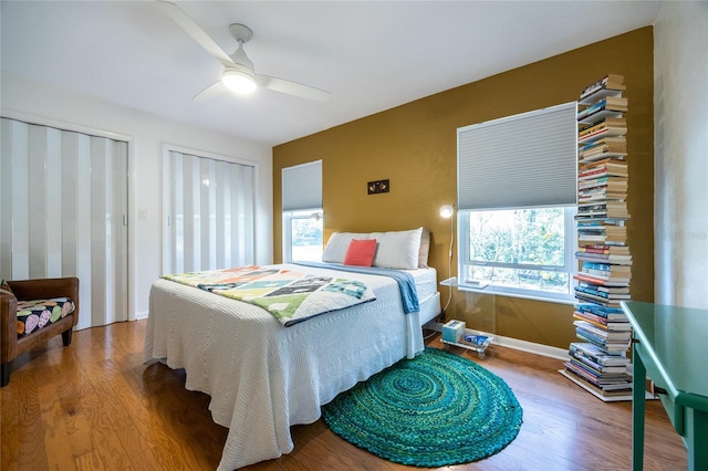 bedroom featuring two closets, ceiling fan, and wood finished floors