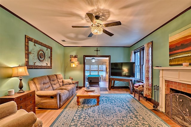 living area featuring ceiling fan, a fireplace, light wood-style flooring, and crown molding