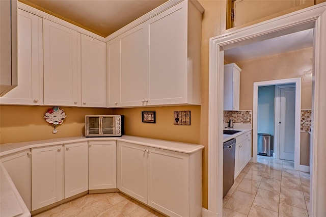 kitchen featuring decorative backsplash, white cabinets, light countertops, and stainless steel dishwasher