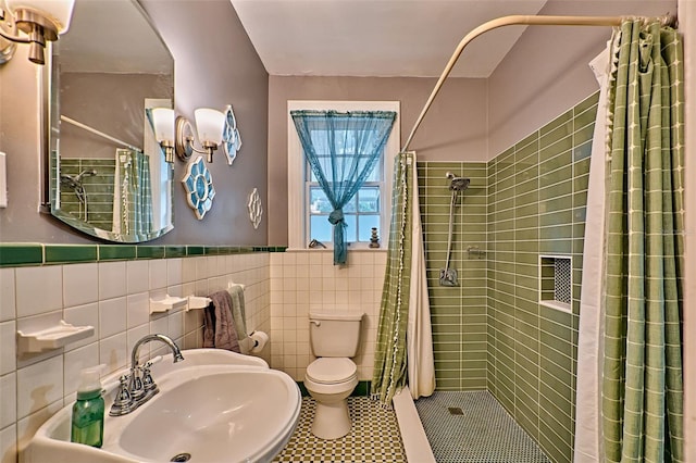 full bathroom featuring toilet, a wainscoted wall, a sink, tile walls, and a shower stall