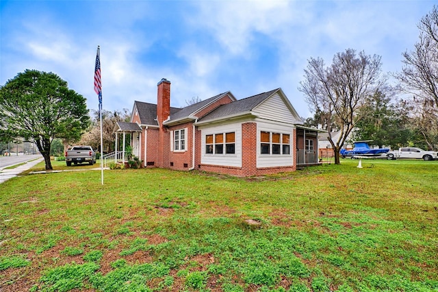 view of side of home with crawl space, brick siding, a yard, and a chimney