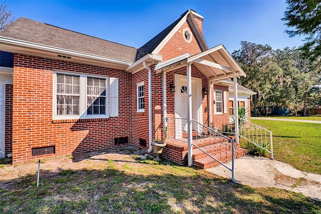 bungalow featuring brick siding, a chimney, a front lawn, and roof with shingles