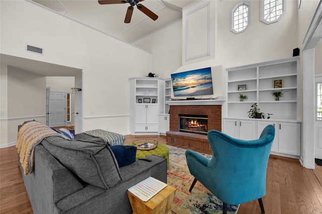 living room featuring light wood-type flooring, visible vents, high vaulted ceiling, a fireplace, and baseboards