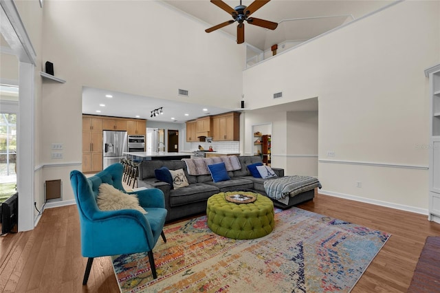 living room with a ceiling fan, visible vents, baseboards, and light wood-type flooring