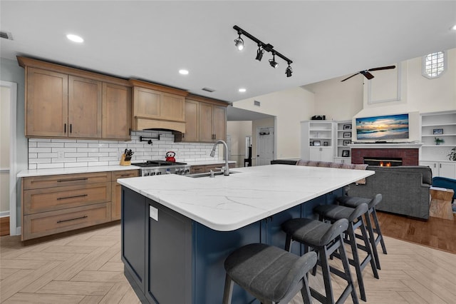 kitchen featuring decorative backsplash, a large island with sink, a fireplace, range, and a sink