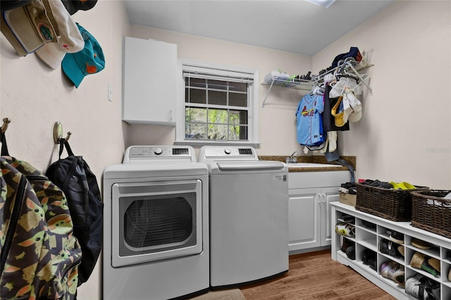 clothes washing area with a sink, cabinet space, wood finished floors, and washing machine and clothes dryer