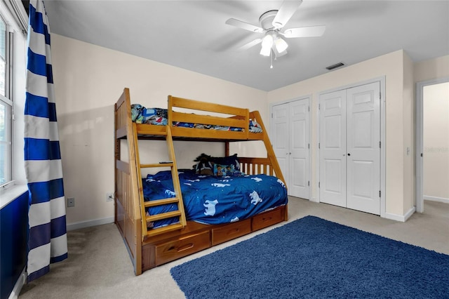 carpeted bedroom with baseboards, visible vents, ceiling fan, multiple windows, and two closets