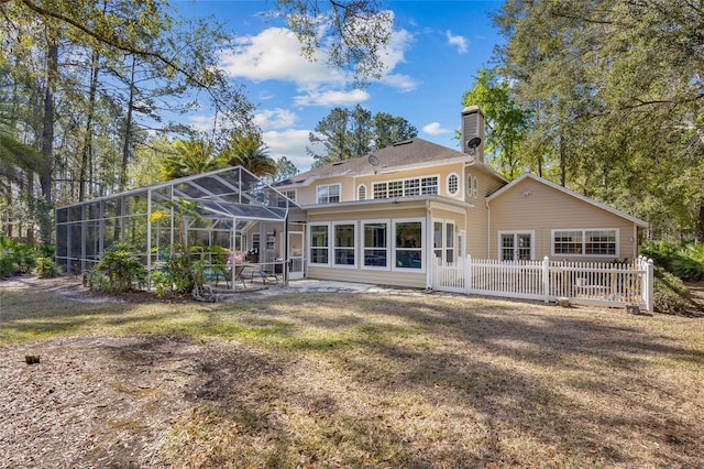 back of property with fence, glass enclosure, a lawn, a chimney, and a patio area