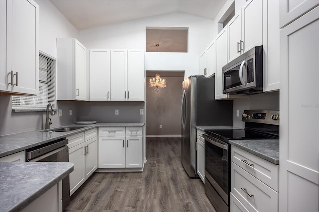 kitchen featuring white cabinets, dark wood-style floors, appliances with stainless steel finishes, vaulted ceiling, and a sink