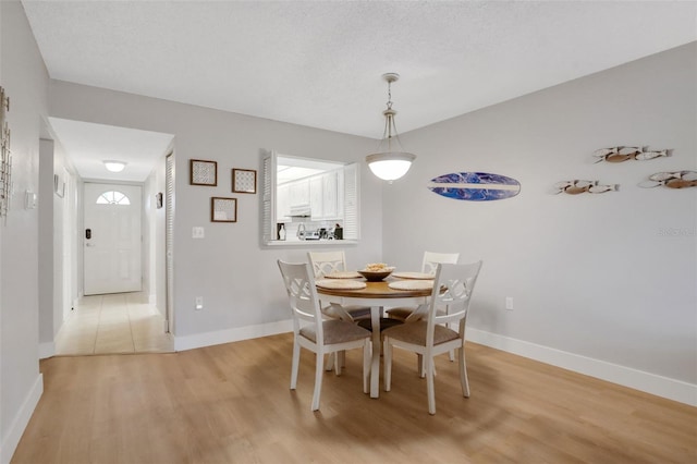 dining area featuring light wood finished floors, baseboards, and a textured ceiling