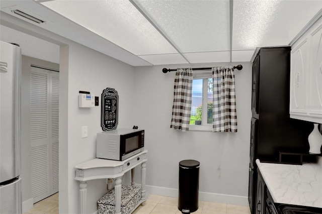 kitchen with light tile patterned floors, freestanding refrigerator, light stone counters, and visible vents