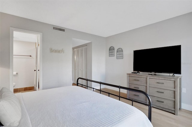 bedroom with ensuite bathroom, wood finished floors, visible vents, baseboards, and a closet