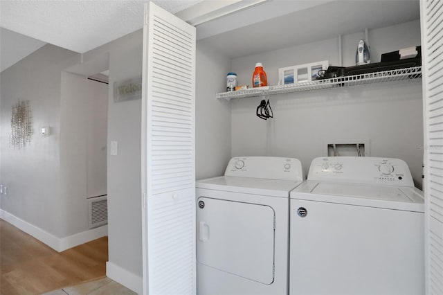 laundry area with laundry area, light wood finished floors, baseboards, visible vents, and washing machine and clothes dryer