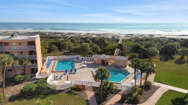 pool with a patio area, a water view, fence, and a view of the beach