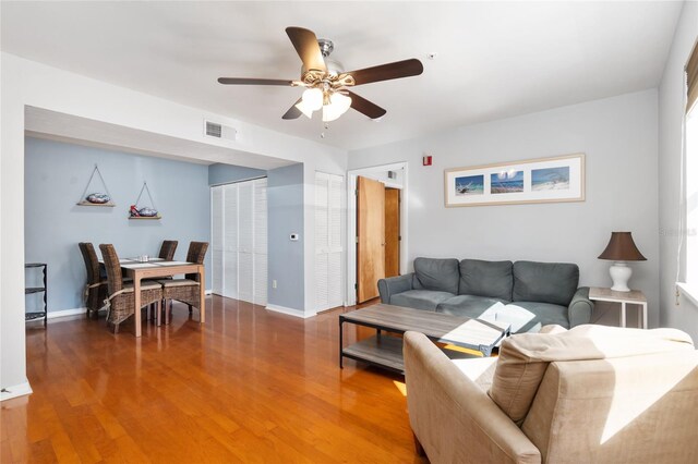 living room featuring ceiling fan, wood finished floors, visible vents, and baseboards