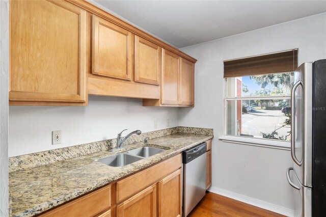 kitchen featuring baseboards, wood finished floors, light stone countertops, stainless steel appliances, and a sink