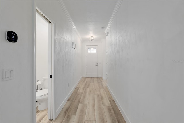 hall featuring baseboards, crown molding, and light wood finished floors