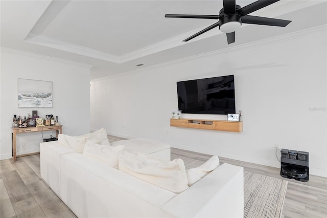 living area featuring light wood finished floors, baseboards, a tray ceiling, and ornamental molding