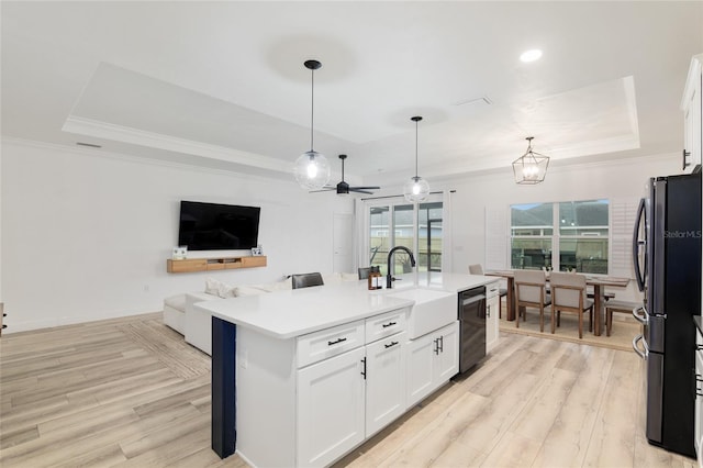 kitchen with a tray ceiling, light countertops, open floor plan, an island with sink, and dishwasher