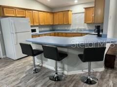 kitchen featuring lofted ceiling, white appliances, light wood-style flooring, and a kitchen bar