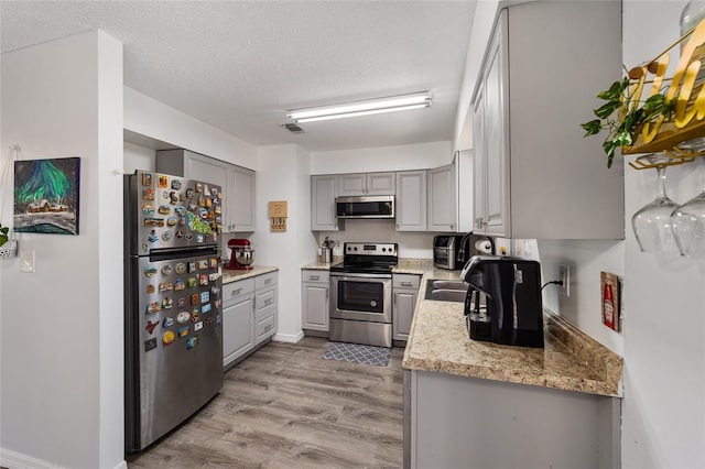 kitchen featuring a textured ceiling, gray cabinetry, stainless steel appliances, visible vents, and light wood finished floors