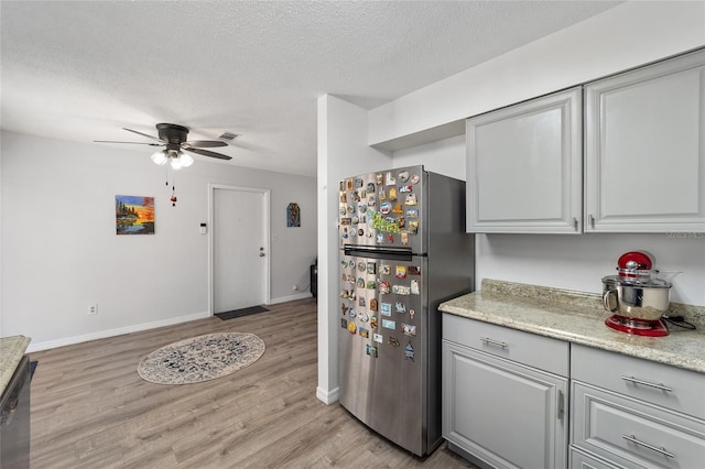 kitchen with a textured ceiling, light wood finished floors, freestanding refrigerator, and baseboards