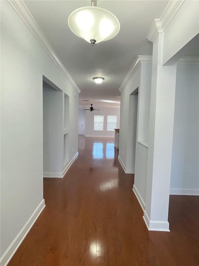 hallway featuring built in features, dark wood-style floors, baseboards, and crown molding