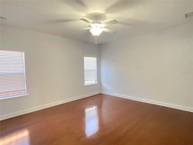 empty room featuring dark wood-type flooring, a ceiling fan, and baseboards