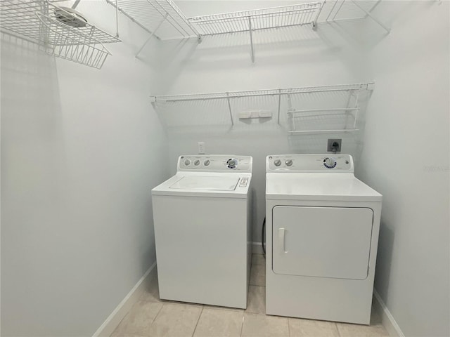 clothes washing area featuring light tile patterned floors, laundry area, washing machine and clothes dryer, and baseboards