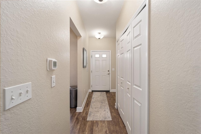 doorway to outside featuring dark wood-style floors, a textured wall, and baseboards