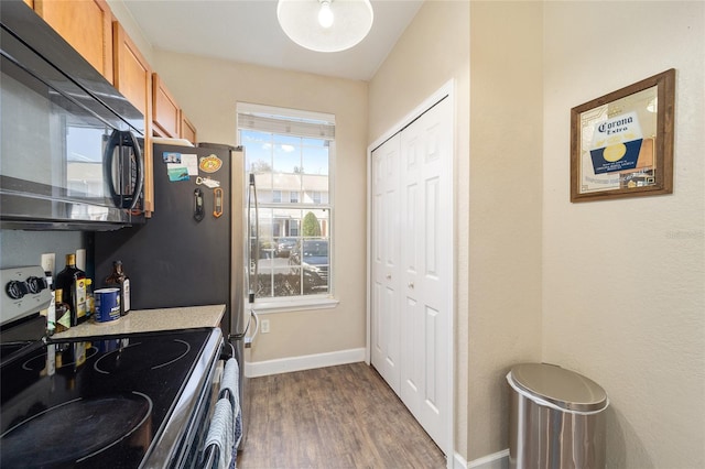 kitchen with brown cabinets, stainless steel electric stove, dark wood-type flooring, black microwave, and baseboards