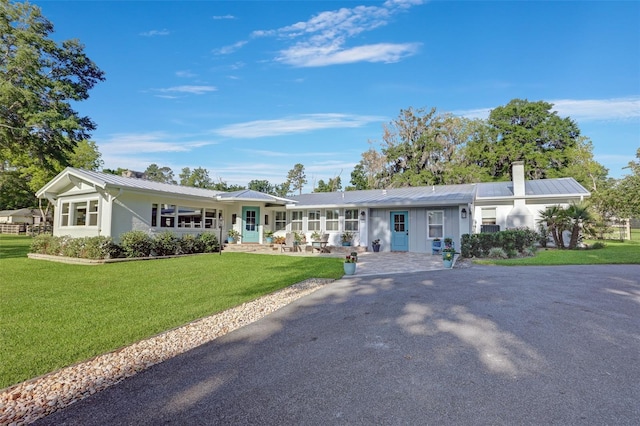 ranch-style home featuring metal roof, a chimney, aphalt driveway, and a front yard