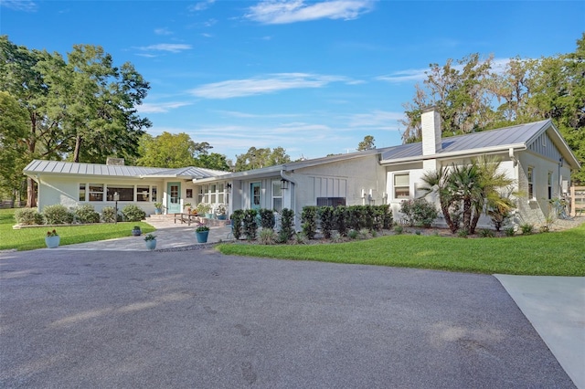 single story home with metal roof, a standing seam roof, a chimney, and a front lawn