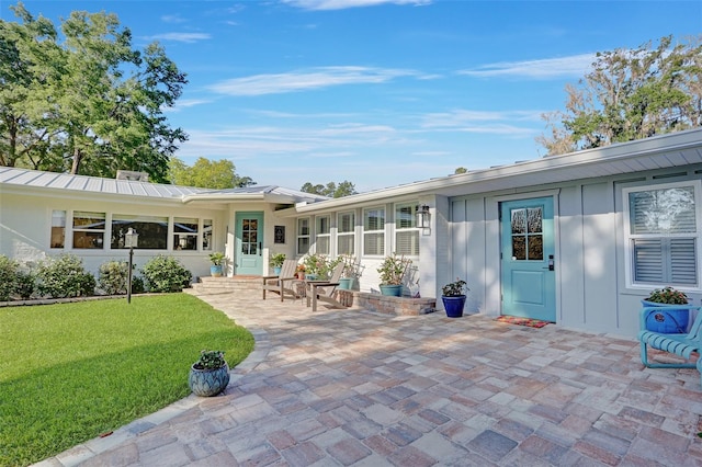 rear view of property with a standing seam roof, metal roof, a patio, and a yard