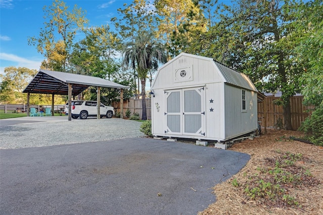 view of shed with driveway, a carport, and fence