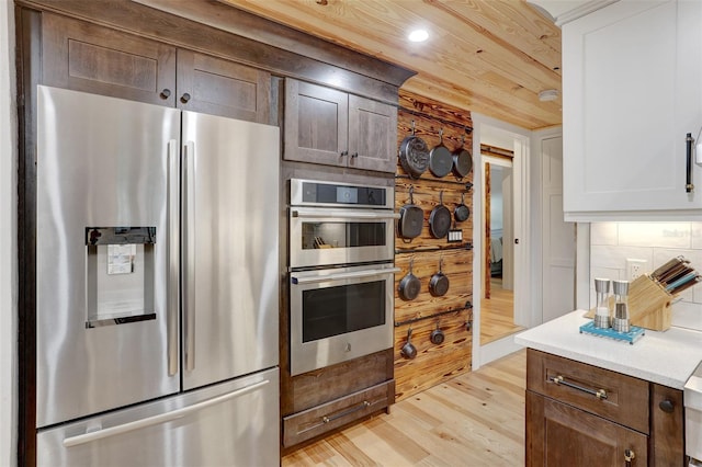 kitchen with tasteful backsplash, wooden ceiling, stainless steel appliances, light countertops, and light wood-style floors