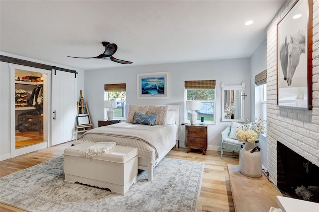 bedroom with light wood finished floors, a barn door, multiple windows, and a fireplace