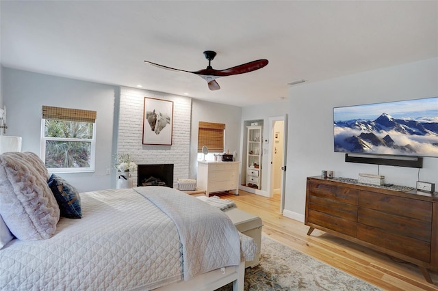 bedroom featuring visible vents, light wood-style flooring, a brick fireplace, ceiling fan, and baseboards