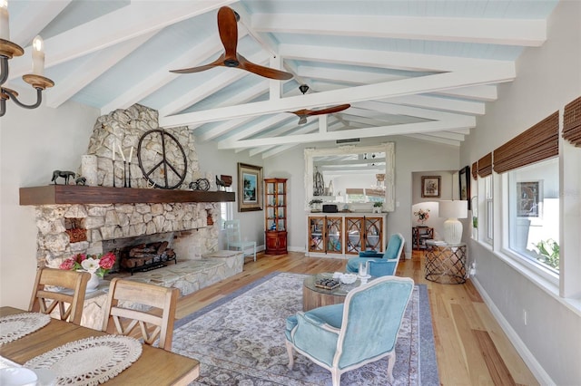 living area featuring vaulted ceiling with beams, a fireplace, a ceiling fan, wood finished floors, and baseboards