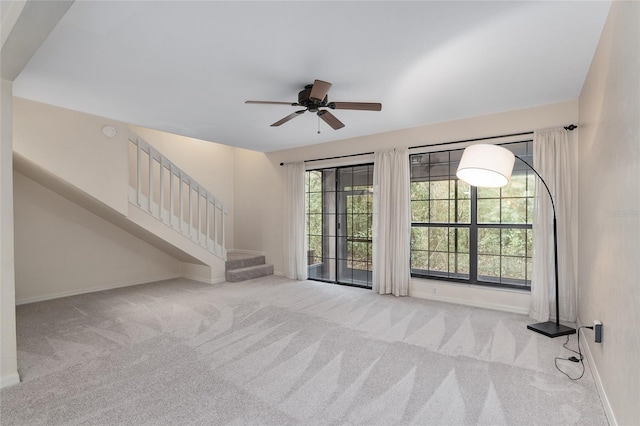 unfurnished living room with baseboards, stairway, a ceiling fan, and light colored carpet