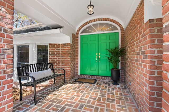 entrance to property featuring brick siding and roof with shingles