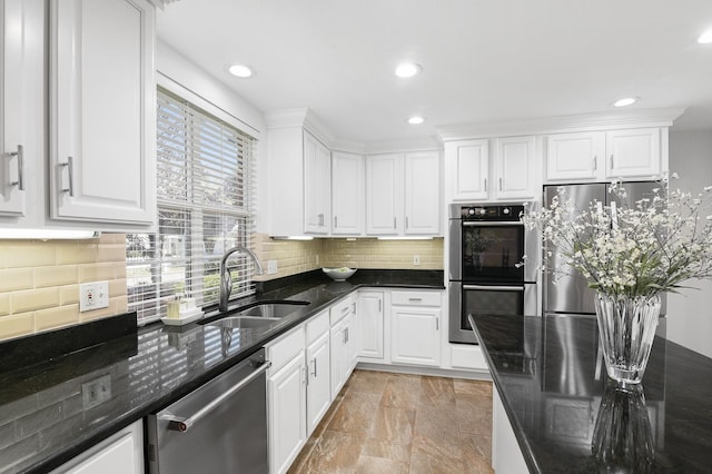 kitchen with dark stone countertops, a sink, stainless steel appliances, white cabinets, and tasteful backsplash