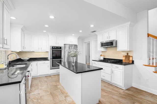 kitchen featuring visible vents, a kitchen island, dark countertops, white cabinetry, and stainless steel appliances